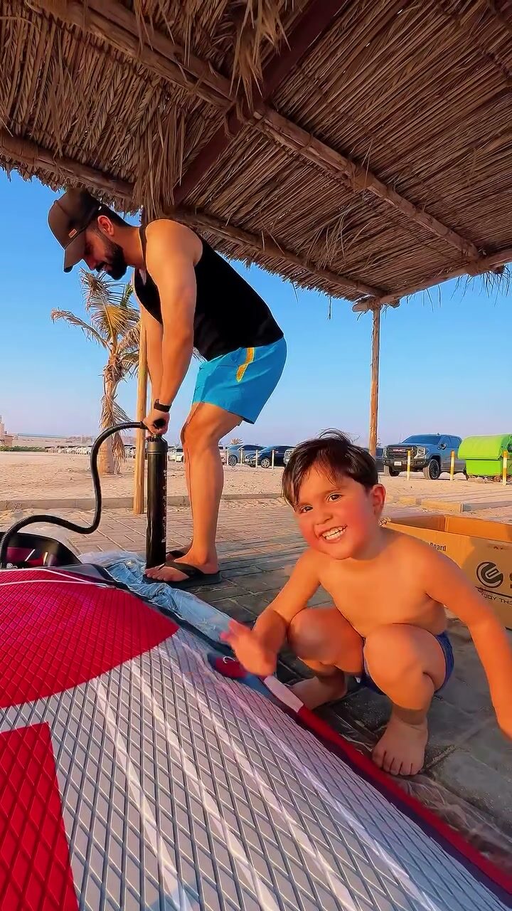 Instructor inflating a board while a child smiles under a beach cabana